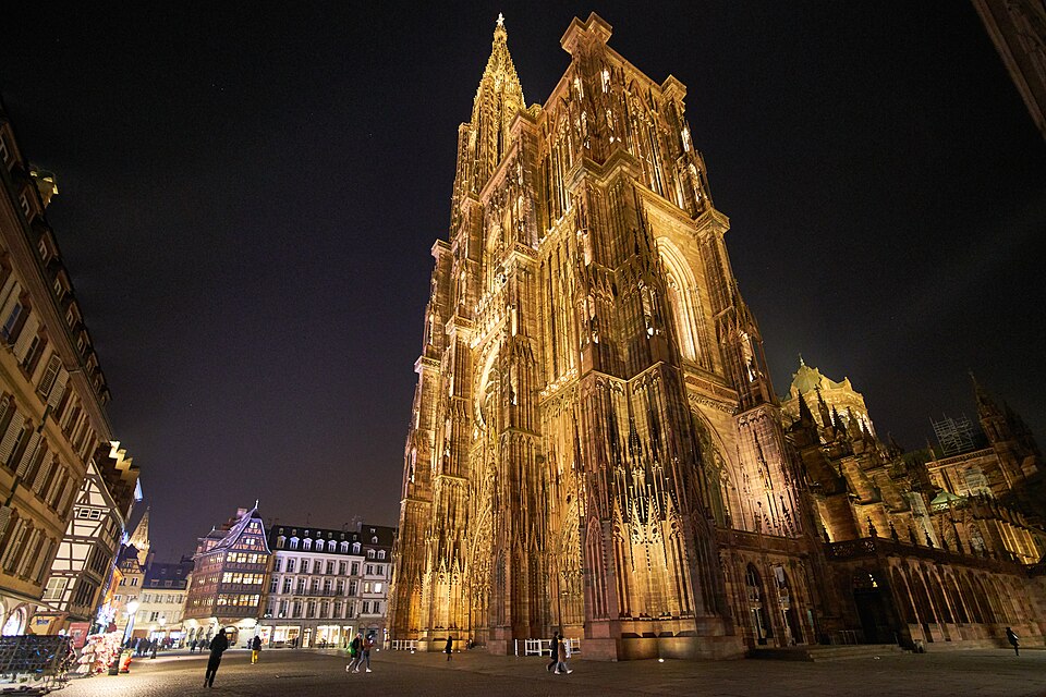 The cathedral's west front and single spire, floodlit against a night sky